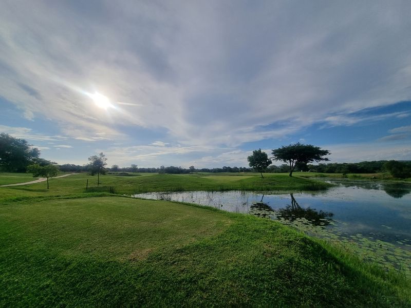 A scenic view of a natural pond surrounded by manicured green lawns and mature trees on a residential estate.