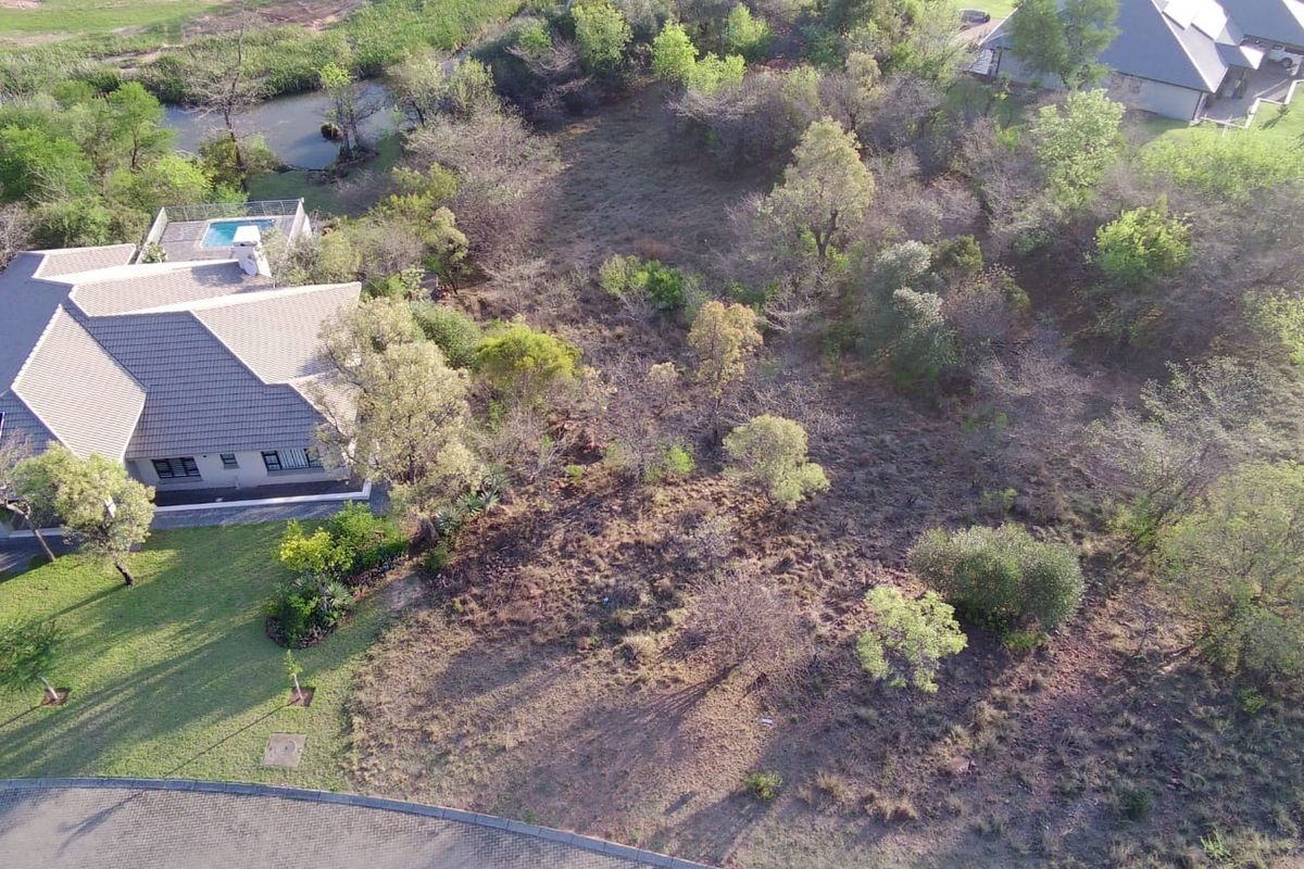 Aerial view of a vacant residential plot featuring established trees and proximity to existing residential infrastructure and a paved road.