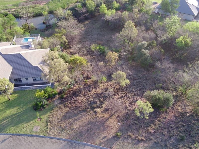 Aerial view of a vacant residential plot featuring established trees and proximity to existing residential infrastructure and a paved road.