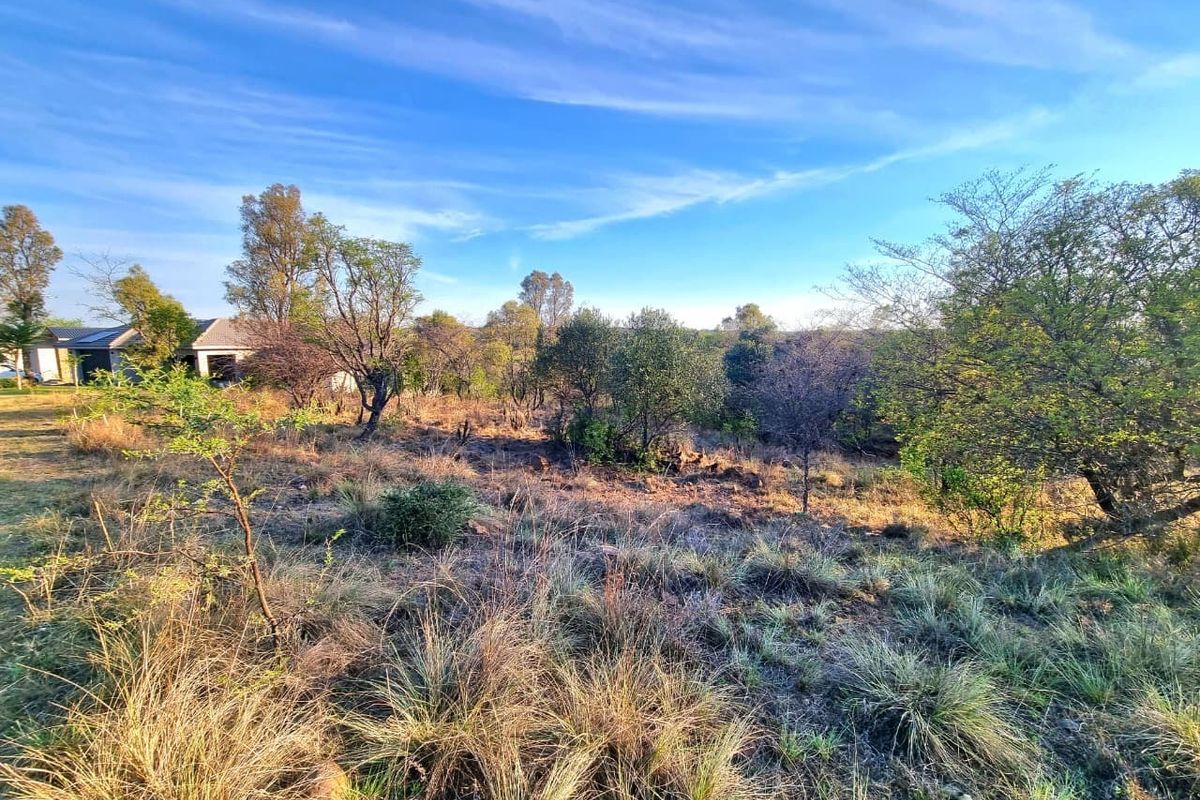 A view of the vacant residential land featuring natural vegetation and sloped terrain, with neighboring properties visible in the distance.