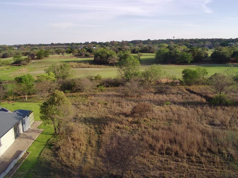 Aerial view of a residential vacant land plot featuring natural vegetation, a paved patio area, and adjacent golf course views.