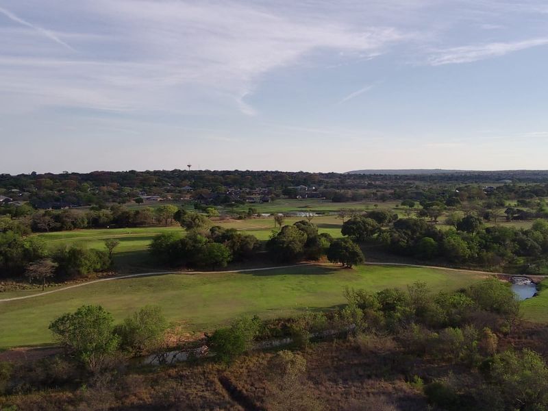 An aerial view of a sprawling residential golf estate featuring lush green fairways, mature trees, and natural water features.