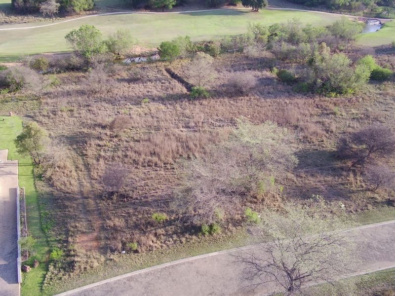Aerial view of a vacant residential plot situated adjacent to a golf course, featuring natural vegetation and access to a paved road.