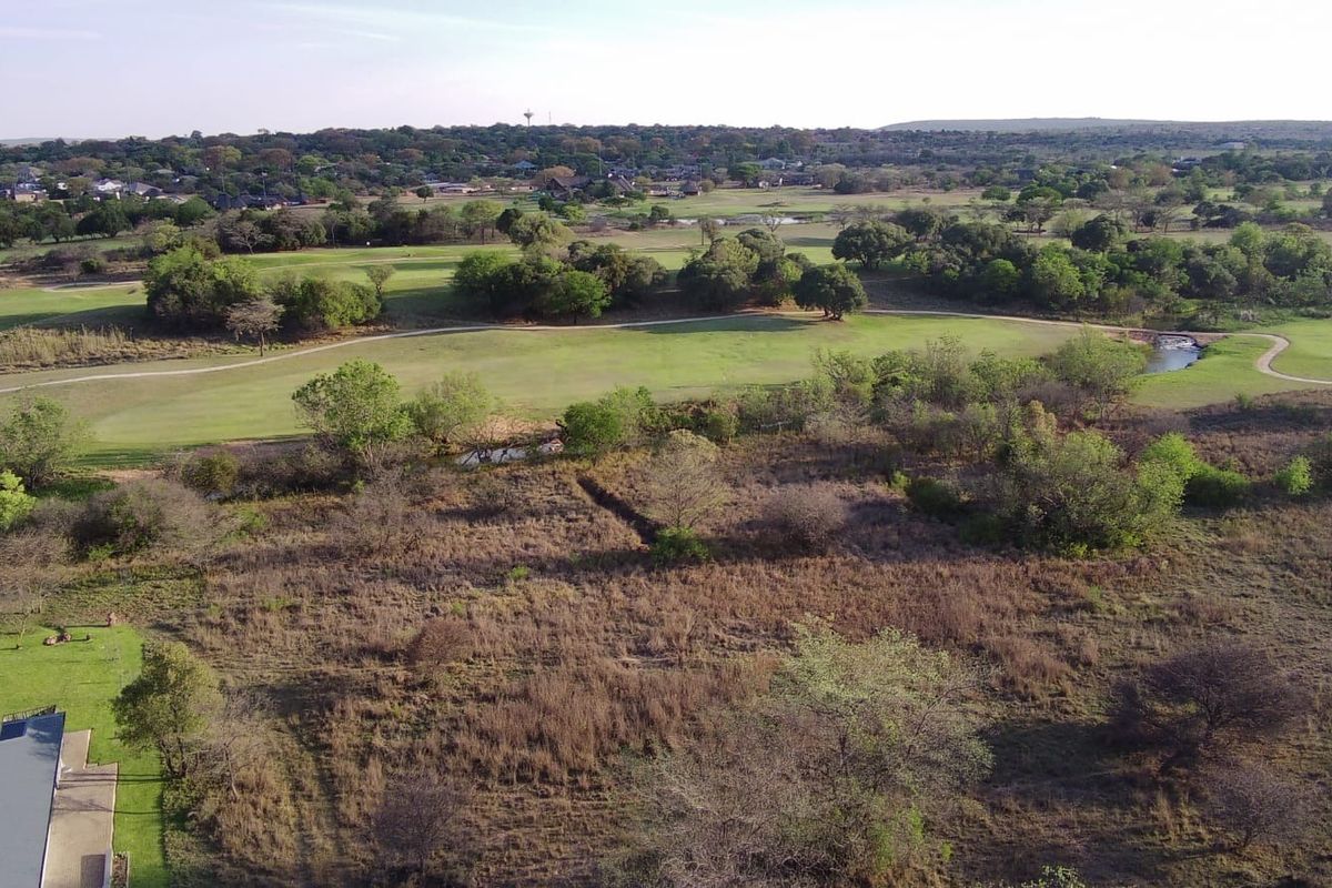 Aerial view of a vacant residential plot featuring natural vegetation, overlooking an adjacent golf course and surrounding landscape.