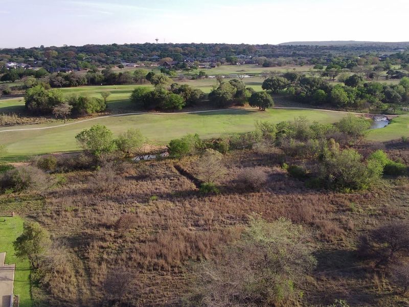 Aerial view of a vacant residential plot featuring natural vegetation, overlooking an adjacent golf course and surrounding landscape.