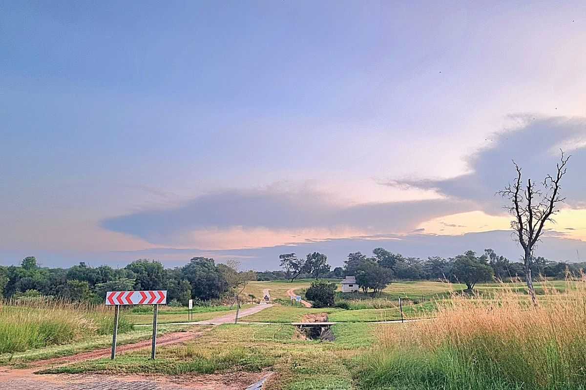 A scenic view of a large, undeveloped residential plot featuring natural grasslands, a dirt access path, and a small drainage culvert.