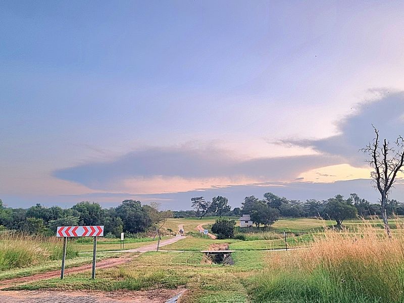 A scenic view of a large, undeveloped residential plot featuring natural grasslands, a dirt access path, and a small drainage culvert.