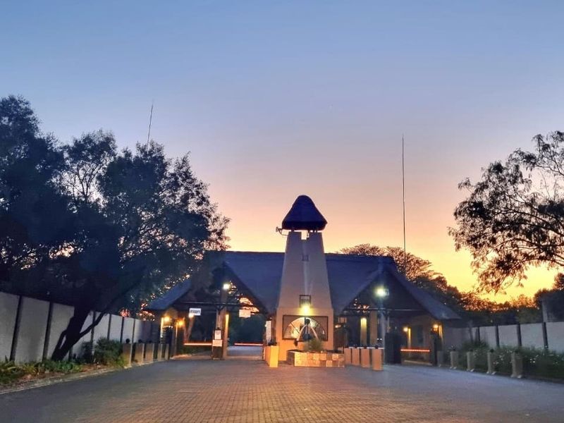 A well-maintained security gatehouse entrance featuring a paved driveway and perimeter wall, captured during sunset.