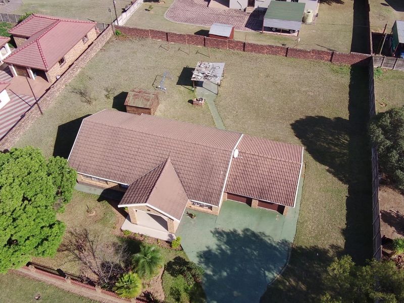 Aerial view of a residential property featuring a tiled roof house, paved driveway, garage, and a large surrounding garden area.