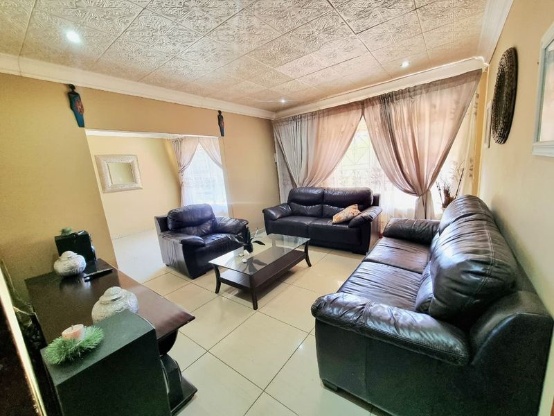 A spacious living room featuring tiled flooring, decorative textured ceiling tiles, and recessed lighting, offering a comfortable and well-defined area for relaxation.