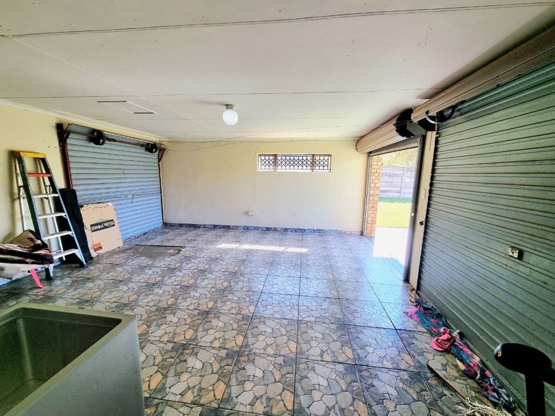 Spacious double garage featuring tiled flooring, dual roller shutter doors, and a built-in utility sink, offering ample storage or parking space.