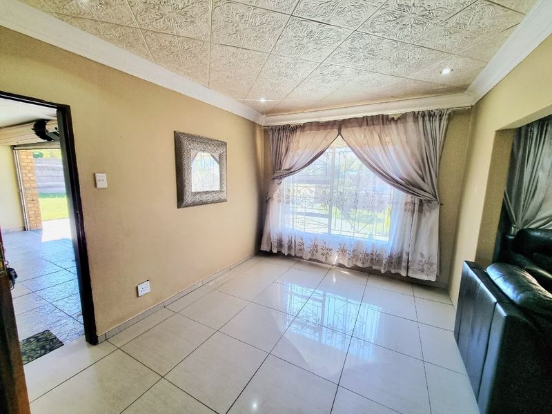 A living room featuring tiled flooring, decorative ceiling tiles, and large windows with security bars, providing access to an adjacent outdoor area.