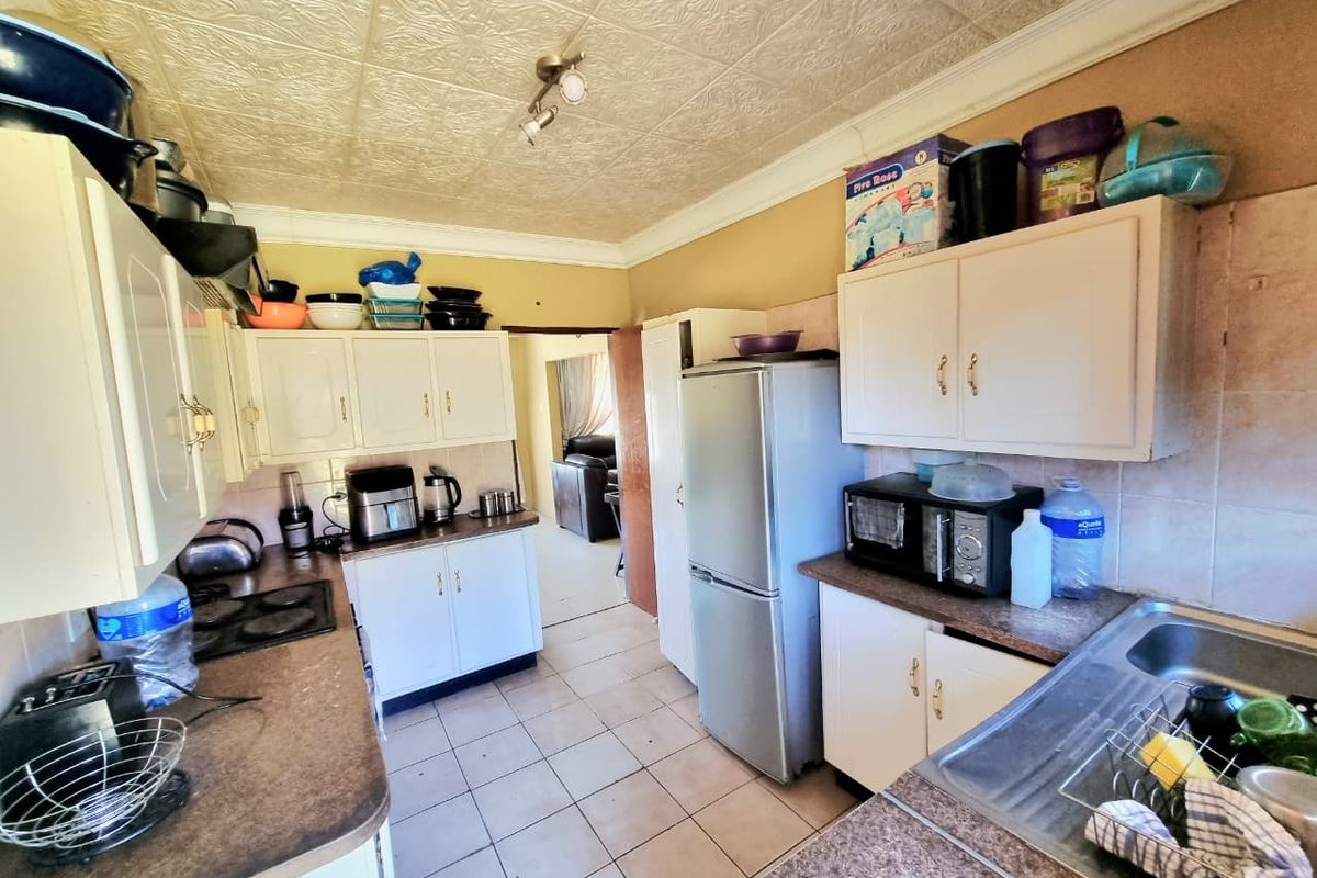 A functional kitchen featuring built-in cabinetry, laminate countertops, an electric hob, and a stainless steel sink, with tiled flooring and a textured ceiling.