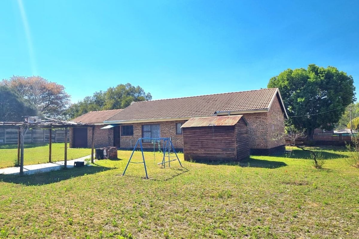 Rear view of a face brick house featuring a tiled roof, security bars on windows, and a spacious backyard with a shed.