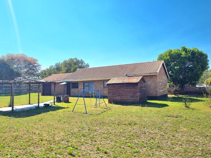 Rear view of a face brick house featuring a tiled roof, security bars on windows, and a spacious backyard with a shed.