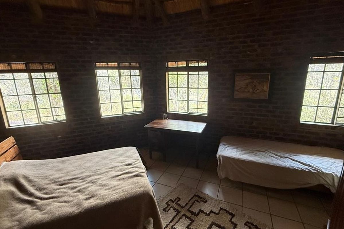 A rustic bedroom featuring exposed brick walls, a traditional thatched ceiling, and tiled flooring, offering a cozy and authentic farm-style atmosphere.