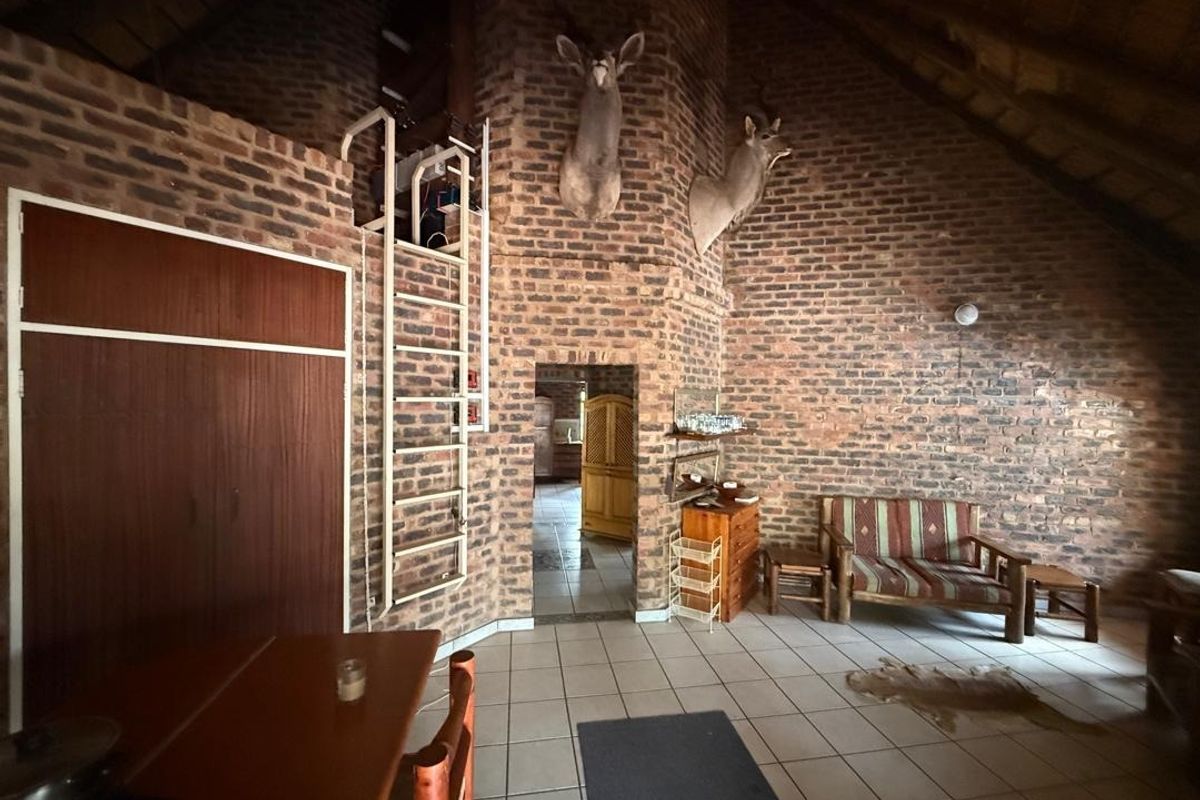 Spacious living area featuring rustic exposed brick walls, vaulted ceilings, and tiled flooring, with a unique built-in ladder leading to an upper level.