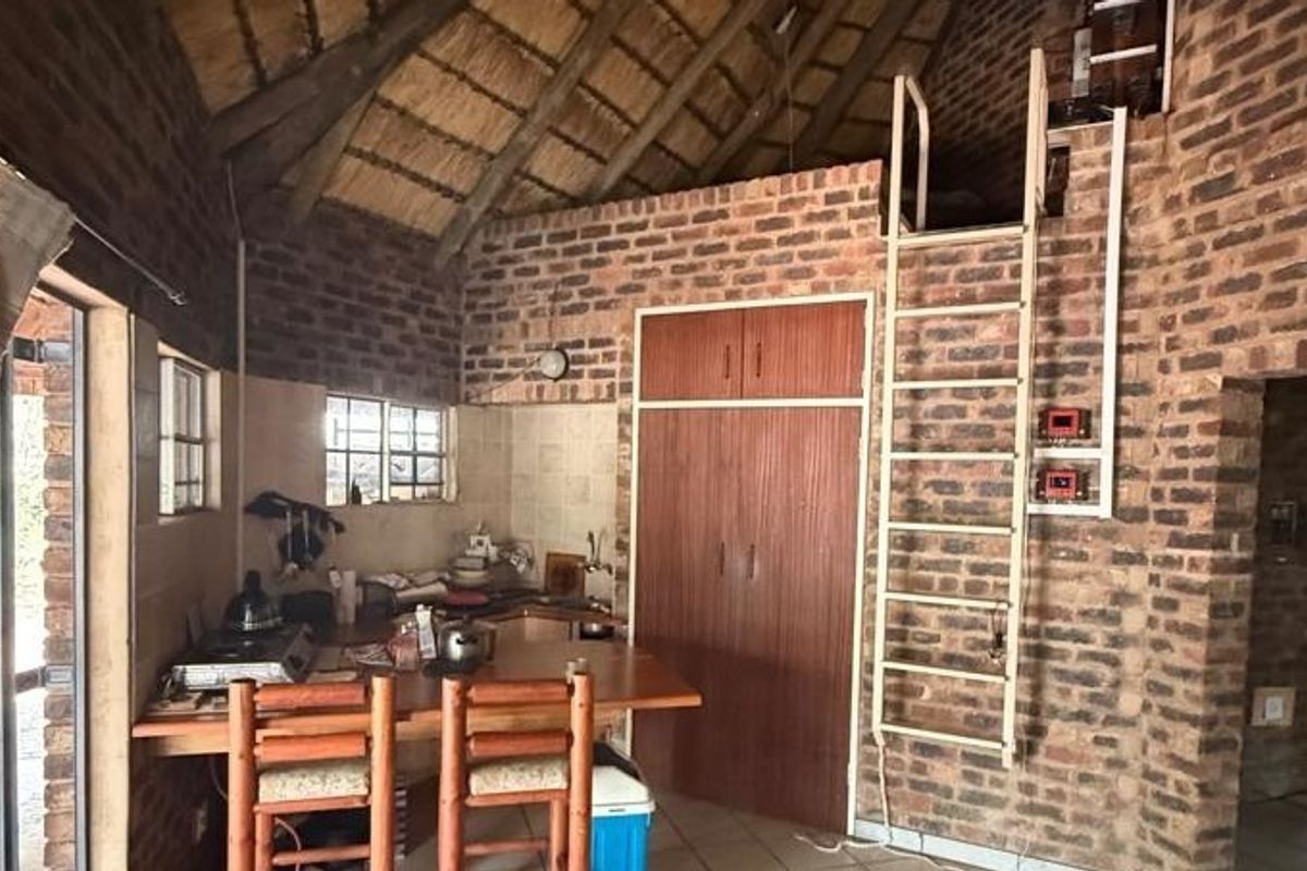 Rustic kitchen featuring exposed brick walls, a high thatched ceiling, built-in cabinetry, and a ladder providing access to an overhead loft area.