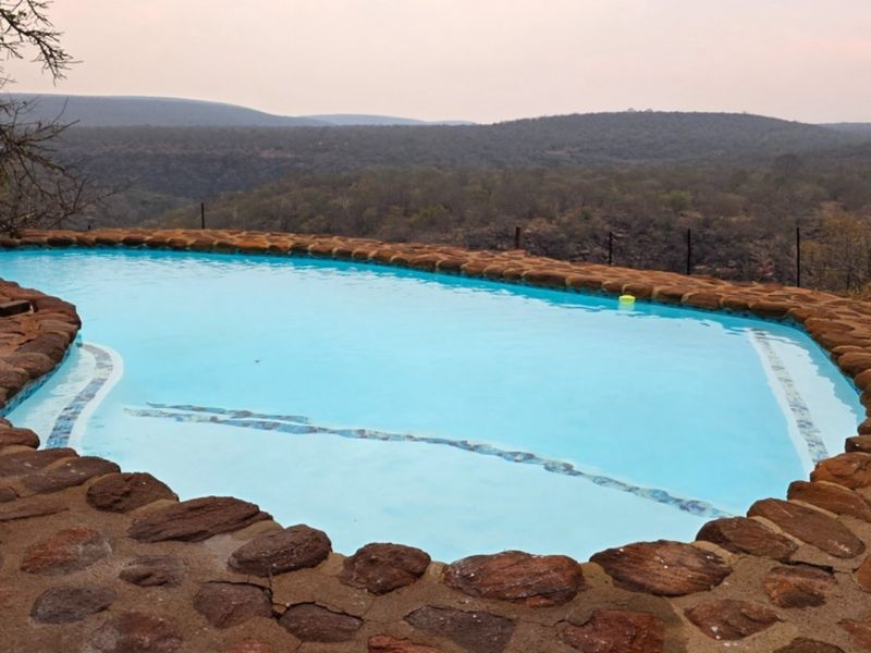 A scenic swimming pool featuring natural stone coping and paving, set against a backdrop of expansive rural landscape views.