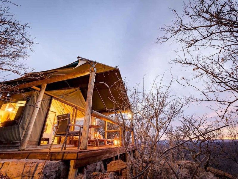 A scenic elevated timber deck featuring a canvas tent structure, offering an immersive outdoor living experience in a natural bushveld setting.