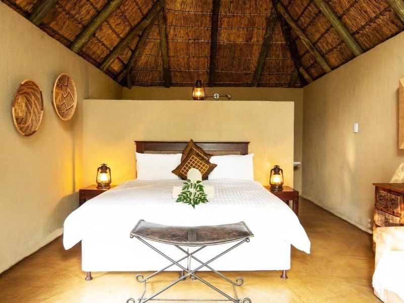 A rustic bedroom featuring a traditional thatched roof with exposed timber rafters and a central partition wall, creating a warm and authentic farm-style atmosphere.