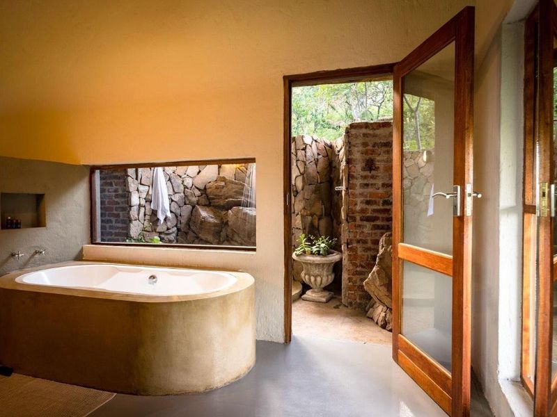 A unique bathroom featuring a built-in concrete bathtub, minimalist wall-mounted fixtures, and direct access to a private, stone-walled outdoor shower area.