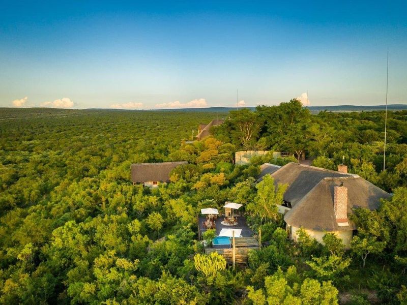 Aerial view of a bushveld property featuring thatched roof structures, a swimming pool, and expansive natural landscape surroundings.