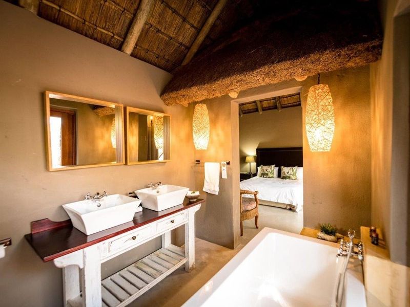 A rustic-style bathroom featuring a double vanity with vessel sinks, a freestanding bathtub, and a traditional thatched roof with exposed timber rafters.
