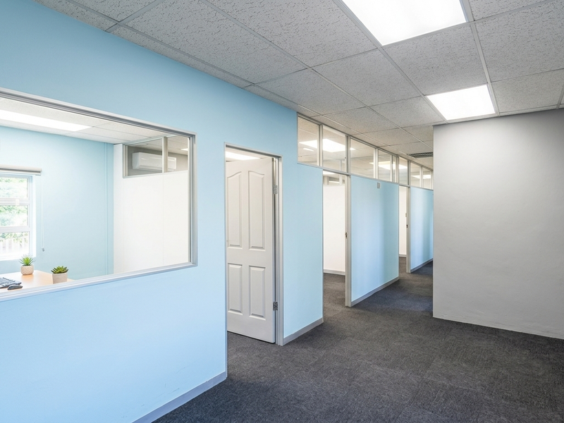 A bright, professional office space featuring glass partitions, suspended ceilings with recessed lighting, and clean carpet flooring, ideal for a modern workspace.