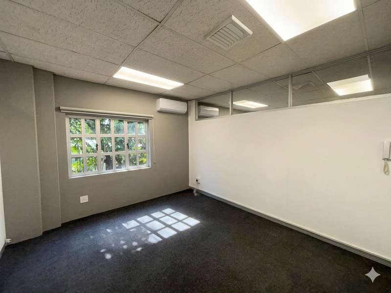 A clean, empty office space featuring a suspended ceiling, recessed lighting, air conditioning, and a glass partition wall, providing a professional work environment.