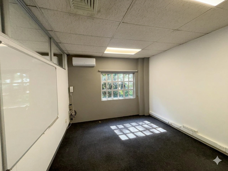 A vacant office space featuring a suspended ceiling, split-system air conditioning, carpeted flooring, and a wall-mounted whiteboard.