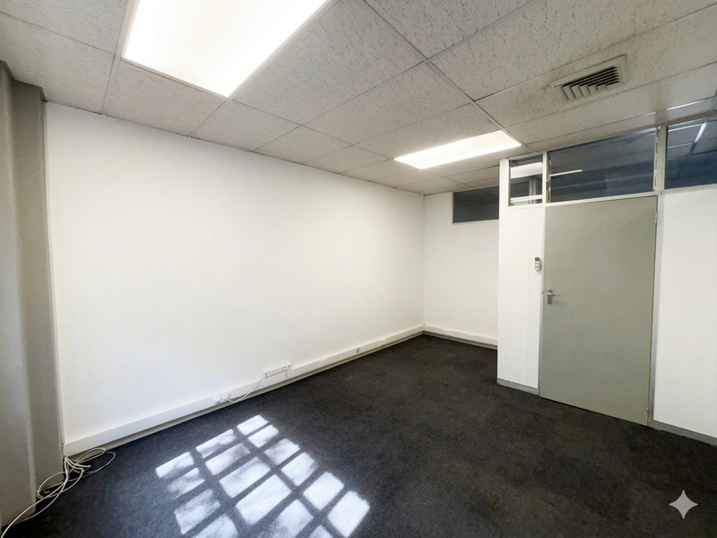 A vacant office space featuring a suspended ceiling with recessed lighting, air conditioning vent, carpet flooring, and an internal glass partition.