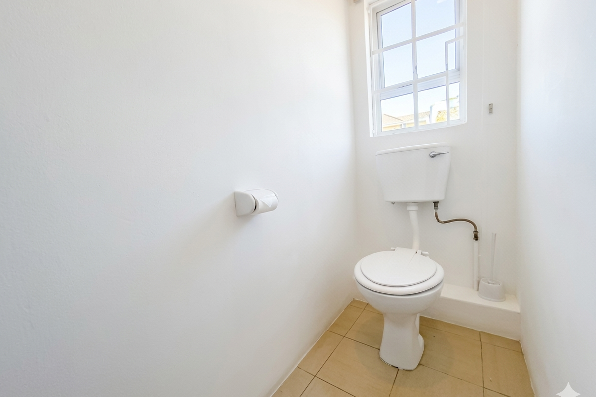 A clean and functional small bathroom featuring a standard toilet, tiled flooring, and a window providing natural light.