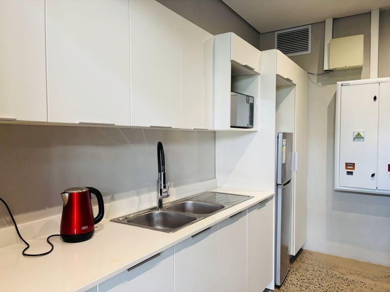 A modern kitchenette featuring white cabinetry, a double sink with a mixer tap, built-in microwave, and an integrated electrical distribution board.