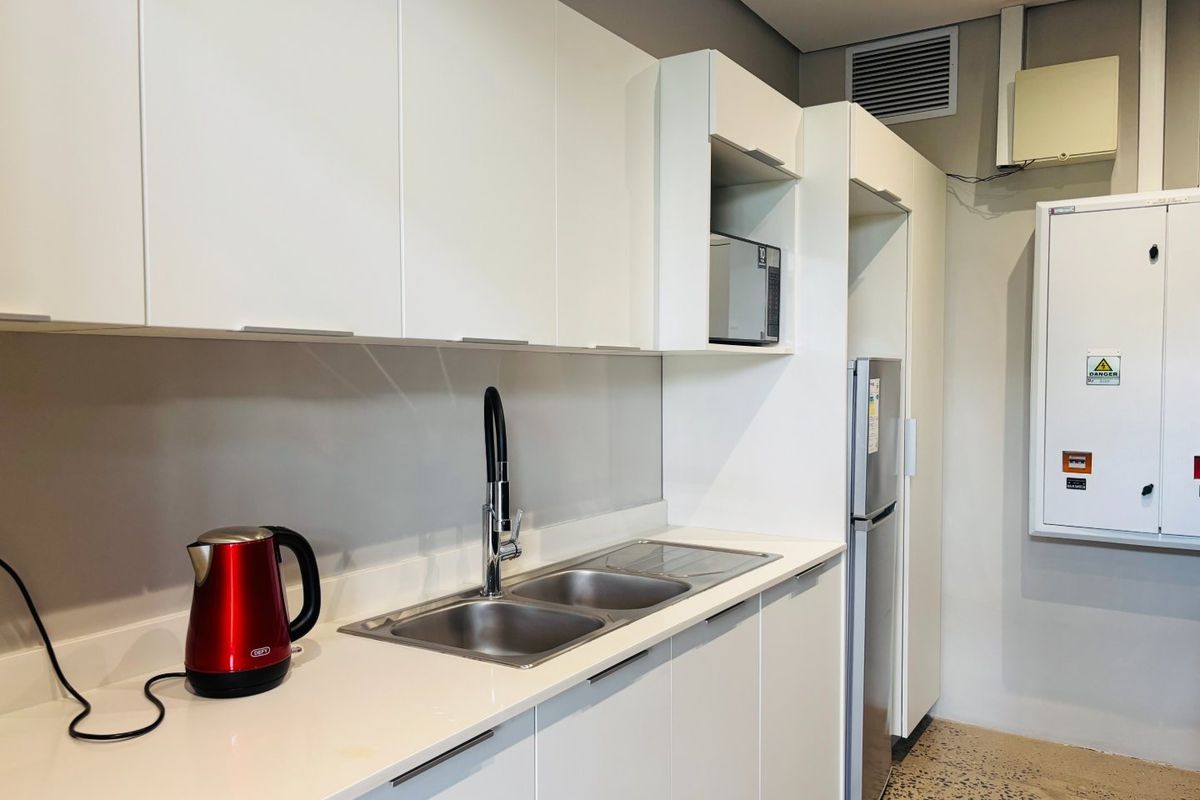 A modern kitchenette featuring white cabinetry, a double sink with a mixer tap, built-in microwave, and an integrated electrical distribution board.
