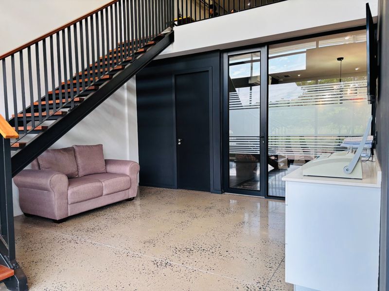 Modern commercial entry area featuring polished concrete floors, a sleek metal staircase with balustrade, and a glass-partitioned office space.