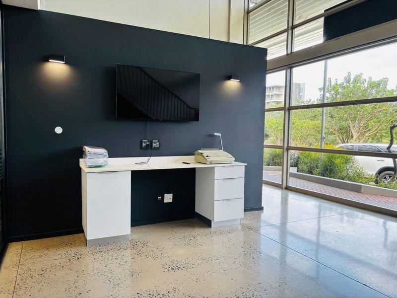 Modern commercial office space featuring a built-in desk, polished concrete floors, and expansive floor-to-ceiling windows providing ample natural light.