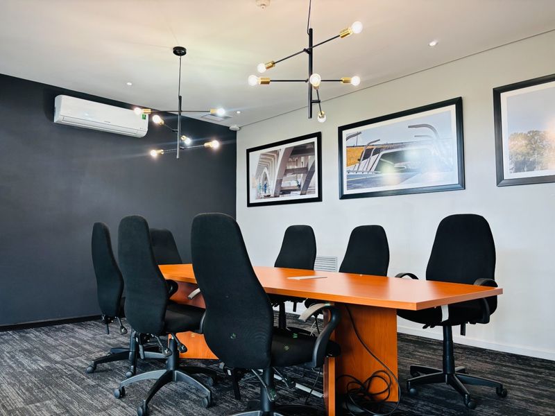 A professional office boardroom featuring a large meeting table, modern pendant lighting, split-system air conditioning, and neutral wall finishes.