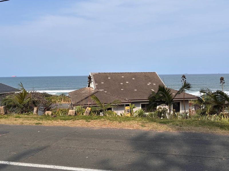 A scenic view of a coastal property featuring a tiled roof house overlooking the ocean.