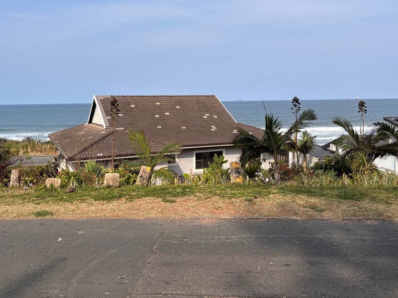 Rear view of a coastal property featuring a tiled roof with visible missing tiles, set against an ocean backdrop.