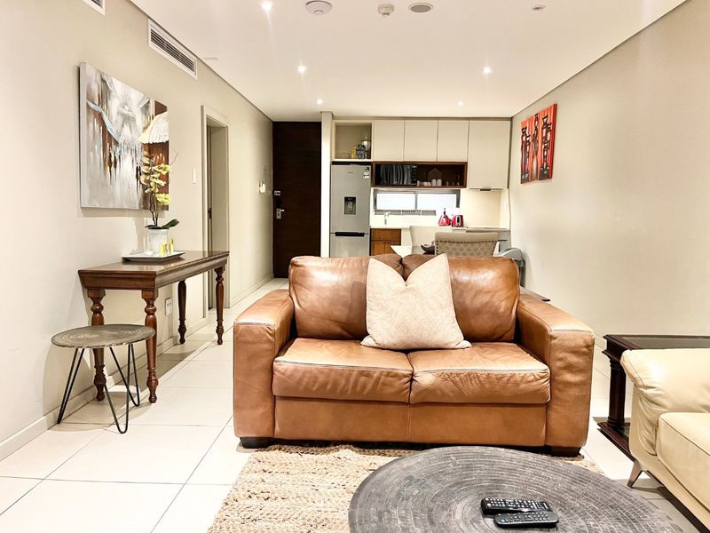An open-plan living area featuring tiled floors, recessed lighting, and a modern kitchen with built-in cabinetry and integrated appliances.