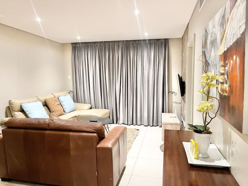 A well-maintained living room featuring neutral tiled flooring, recessed downlighting, and full-length curtain tracks, creating a comfortable and functional living space.