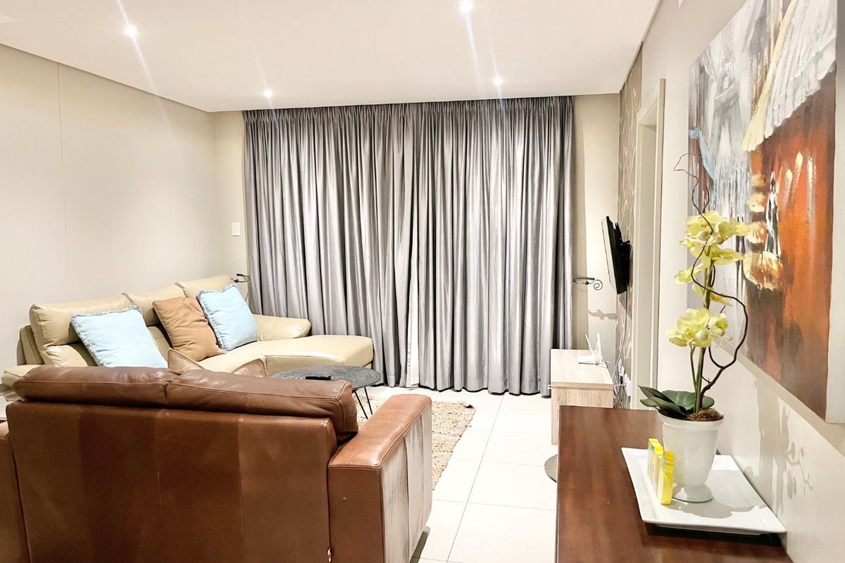 A well-maintained living room featuring neutral tiled flooring, recessed downlighting, and full-length curtain tracks, creating a comfortable and functional living space.