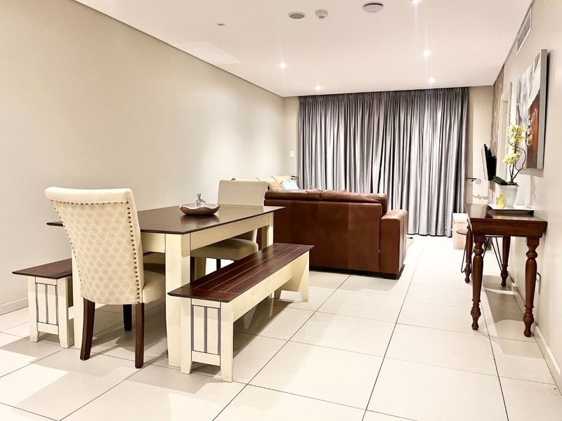 Spacious open-plan living and dining area featuring neutral tiled flooring, recessed downlighting, and full-length window curtains.
