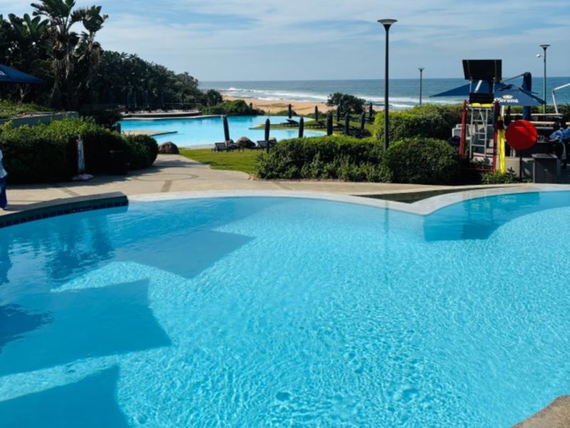 A well-maintained outdoor swimming pool area featuring landscaped gardens and direct views of the nearby coastline.