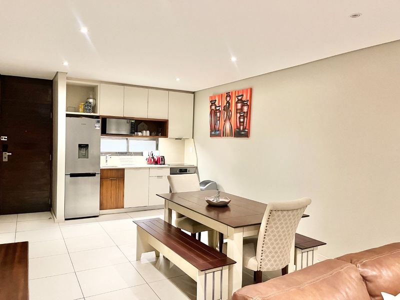 An open-plan living and dining area featuring a modern kitchen with built-in cabinetry, integrated appliances, and neutral tiled flooring.