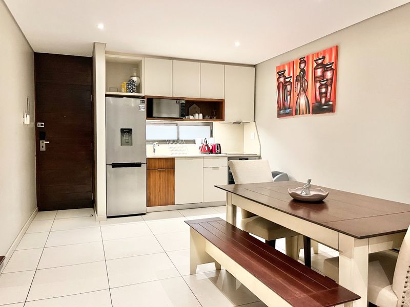 Modern open-plan kitchen and dining area featuring sleek built-in cabinetry, integrated appliances, and neutral tiled flooring in a well-maintained apartment setting.