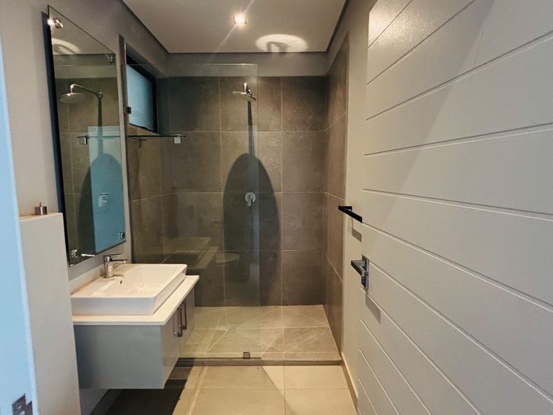 Modern bathroom featuring a wall-mounted vanity, ceramic basin, and a spacious walk-in shower with glass enclosure and contemporary tiling.
