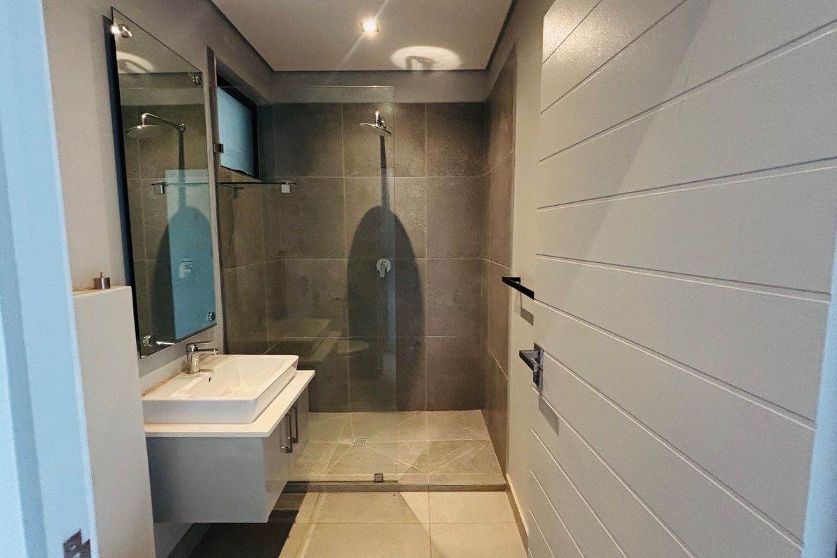 Modern bathroom featuring a wall-mounted vanity, ceramic basin, and a spacious walk-in shower with glass enclosure and contemporary tiling.