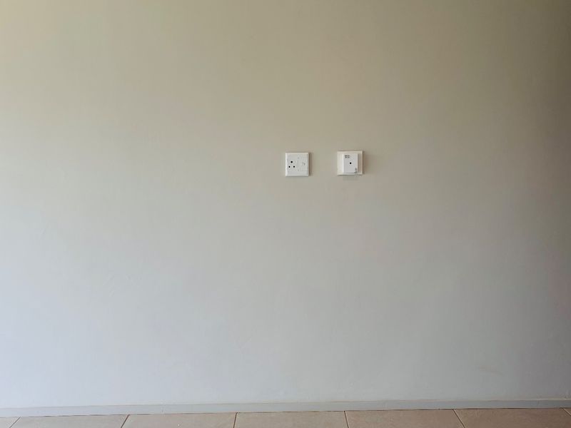 A plain interior wall featuring electrical outlets and tiled flooring, suitable for various living space configurations.
